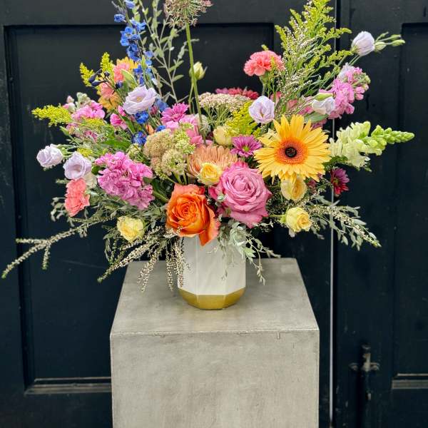 Mixed bouquet in a white vase with pink, yellow, orange, and blue flowers