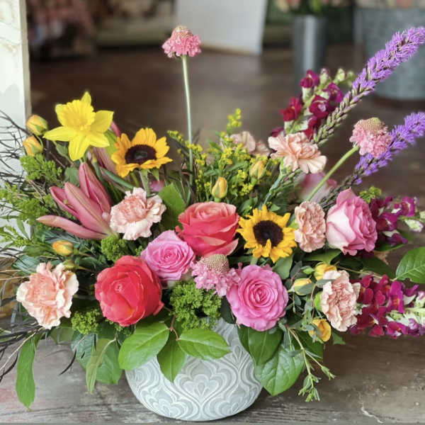 Mixed bouquet in a patterned vase with roses, sunflowers, lilies, and carnations