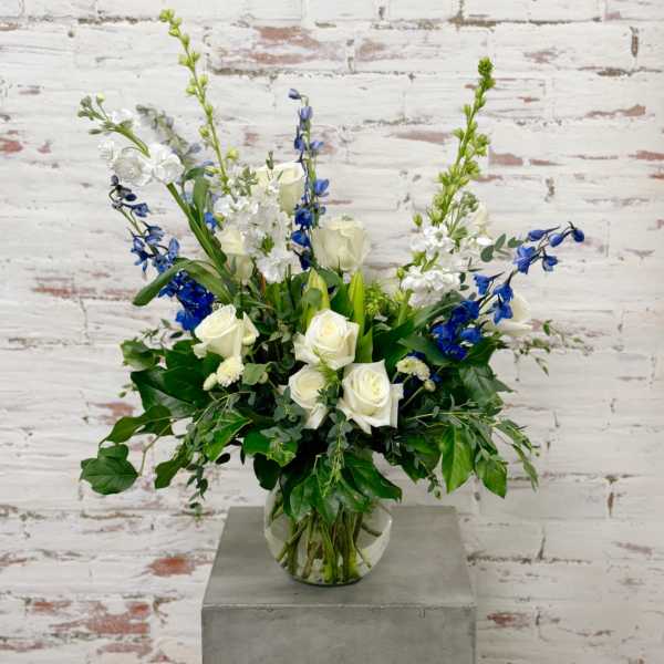 White roses and blue flowers arranged in a clear glass vase