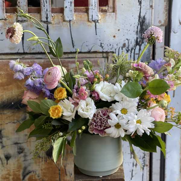 Mixed bouquet in a pale green vase with white, pink, purple, and yellow flowers