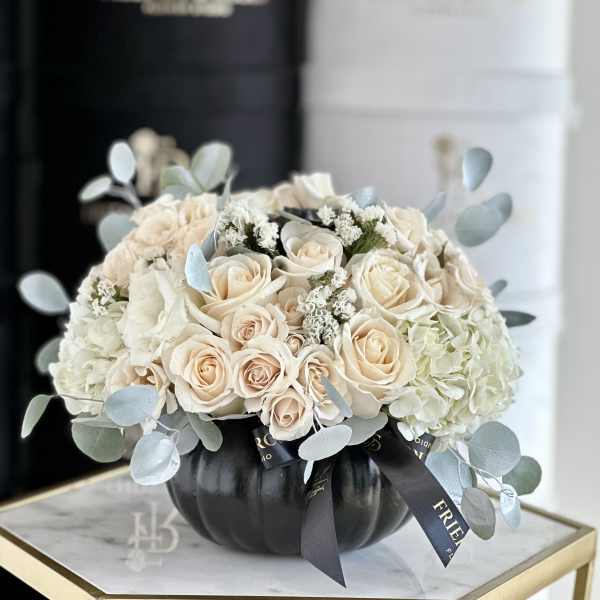 Cream roses and hydrangeas arranged in a black pumpkin vase