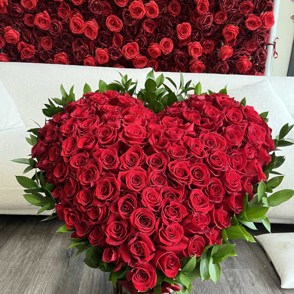 Heart-shaped bouquet of red roses with green foliage and a red ribbon