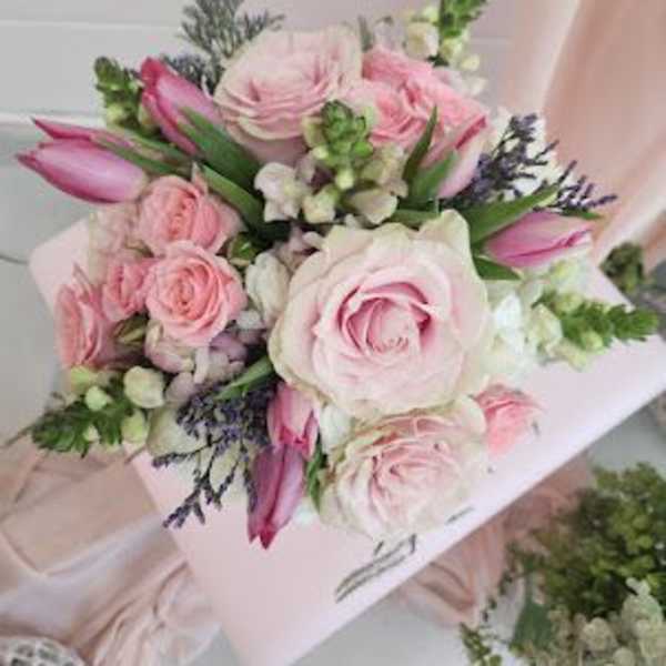 Hand-tied bouquet of soft pink roses, pink tulips, and white blooms in a compact round design
