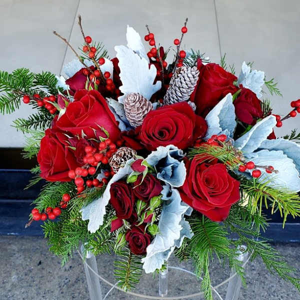 Low centerpiece of red roses with red berries, frosted pinecones, and evergreens in a winter arrangement