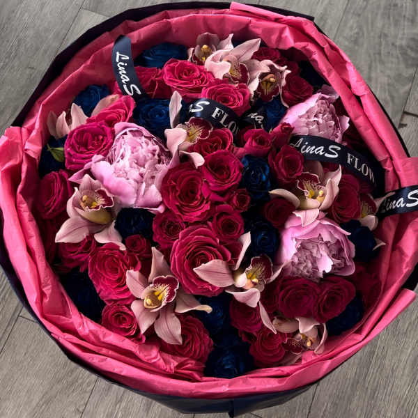 Round bouquet of pink, blue, and pale flowers wrapped in bright pink paper