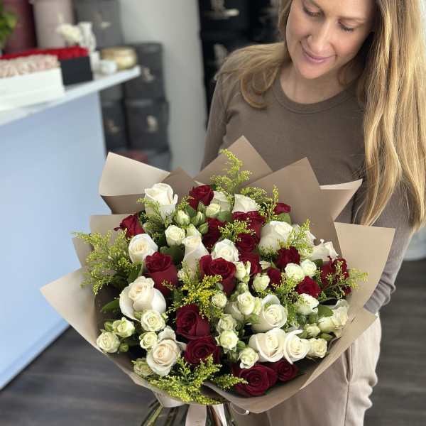 Woman holding a large bouquet of red and white roses wrapped in brown paper.