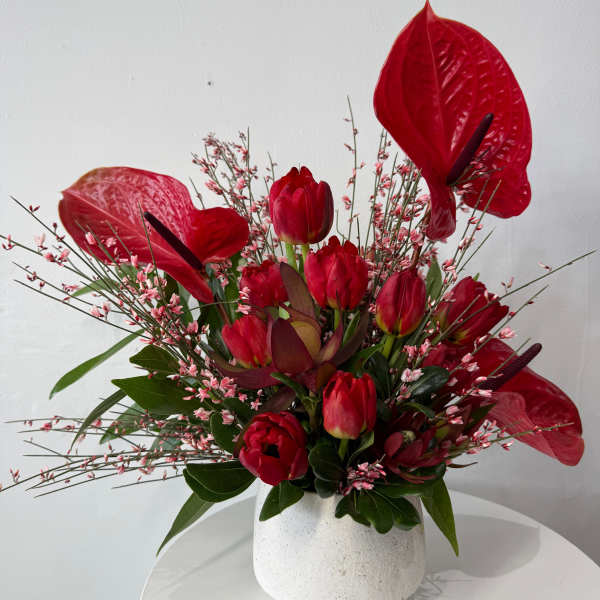 Red anthuriums and tulips arranged in a white vase