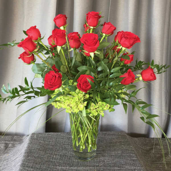 Red roses arranged in a clear glass vase with green filler