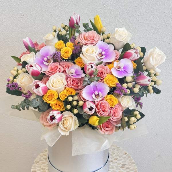 Mixed bouquet of roses, tulips, and orchids in a white hat box