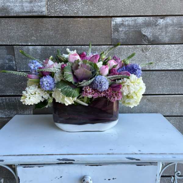 Mixed pink, purple, and white flower arrangement in a dark glass vase