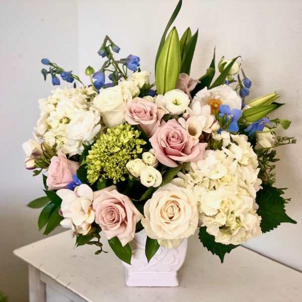 Bouquet of pastel roses, hydrangeas, lilies, and blue flowers in a white vase