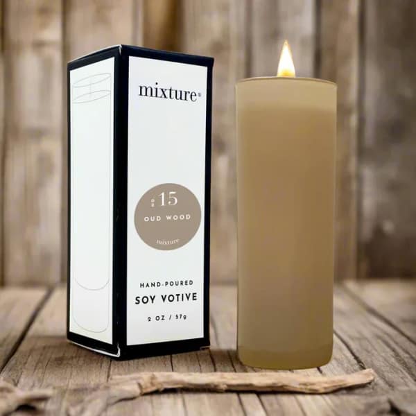 Lit beige soy votive candle beside its box