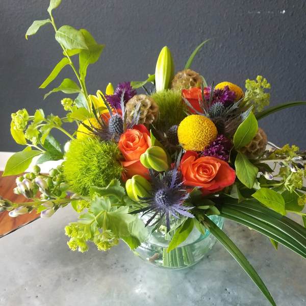 Mixed bouquet with orange roses, yellow blooms, and green accents in a glass vase