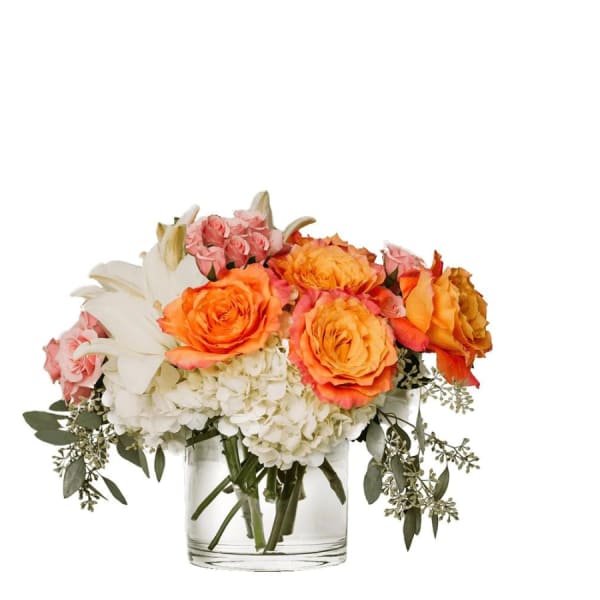Orange and pink roses with white lilies and hydrangeas in a clear glass vase