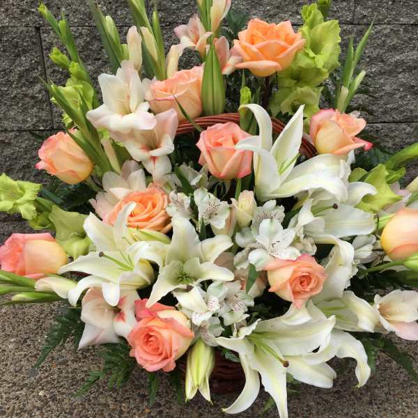 Basket arrangement of peach roses and white lilies with pale green gladiolus