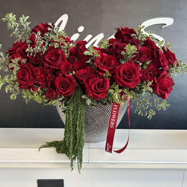 Large red rose arrangement in a silver vase with trailing greenery