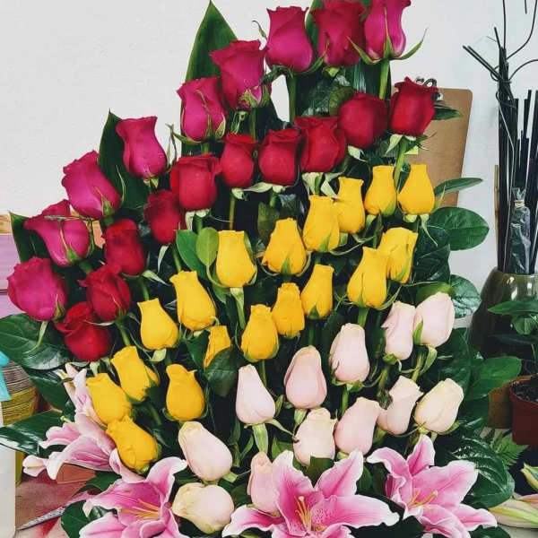 Basket arrangement of roses and pink lilies in red, yellow, and white