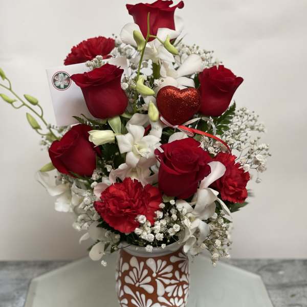 Red roses and white flowers arranged in a patterned vase with a red heart pick