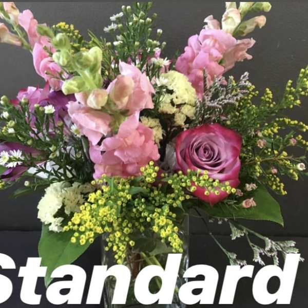 Mixed pink snapdragons and a pink rose with white and yellow accent blooms in a clear vase.