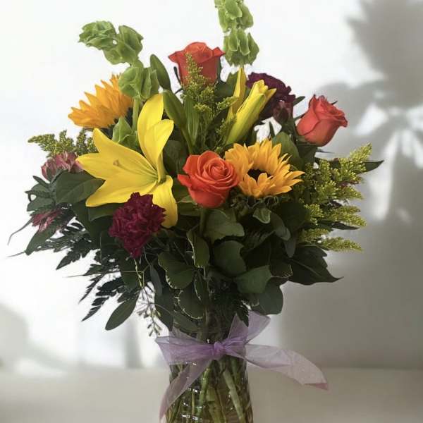 Mixed bouquet of lilies, roses, and sunflowers in a glass vase