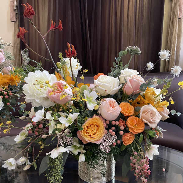 Large mixed bouquet of peach, white, and orange flowers in a metallic vase