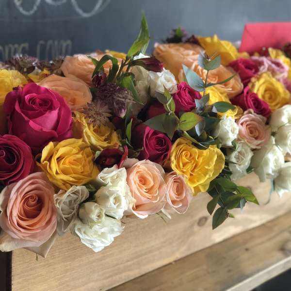 Long box arrangement of roses in pink, yellow, peach, and white