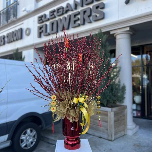 Tall red branch arrangement in a red vase with gold ribbons and hanging ornaments