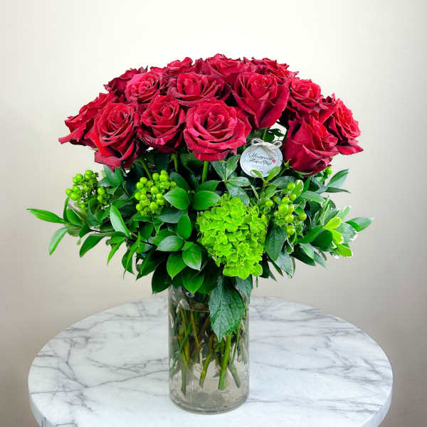 Red roses arranged in a clear glass vase with bright green foliage