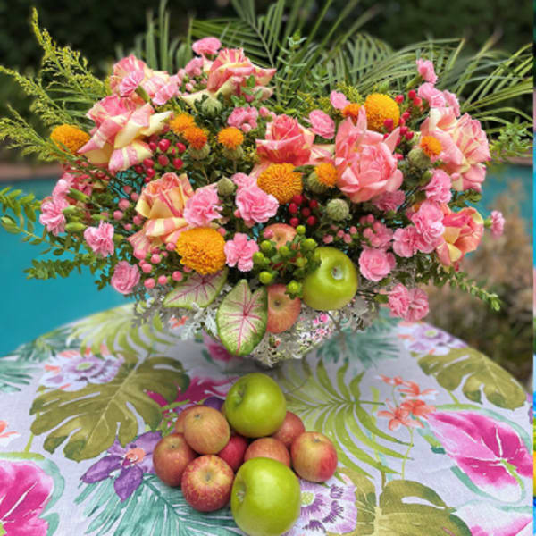 Pink and yellow floral arrangement with apples on a tropical-patterned tablecloth