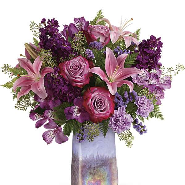 Pink lilies and roses arranged in a tall iridescent vase