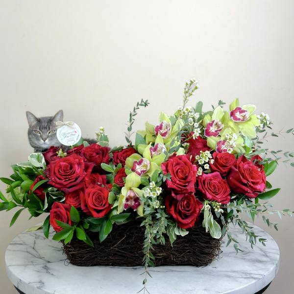 Red roses and green orchids in a woven basket with a cat figurine