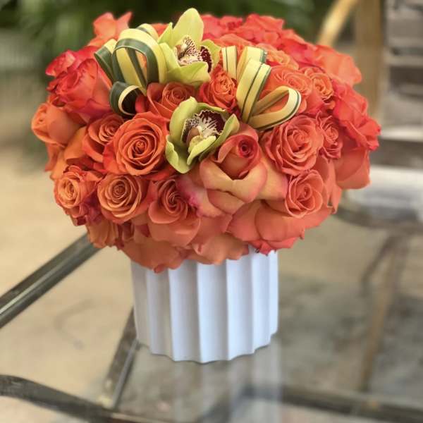 Orange rose bouquet with green orchids in a white vase