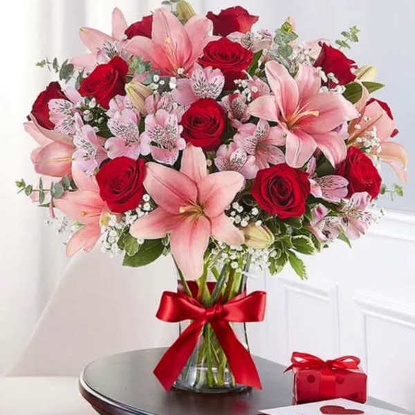 Bouquet of pink lilies and red roses in a glass vase with a red ribbon