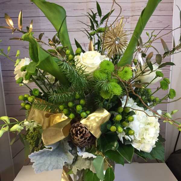 Green and white floral arrangement in a glass vase with gold ribbon