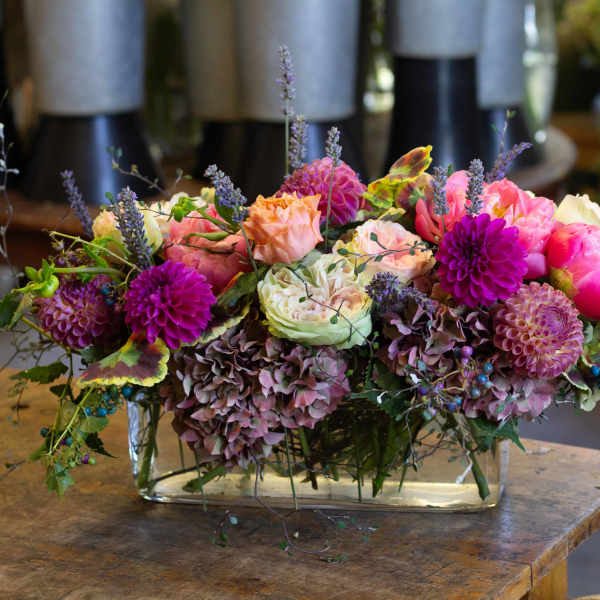 Low floral arrangement with pink, peach, and purple blooms in a glass vase