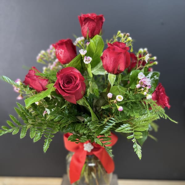 Red roses arranged in a glass vase with a red ribbon