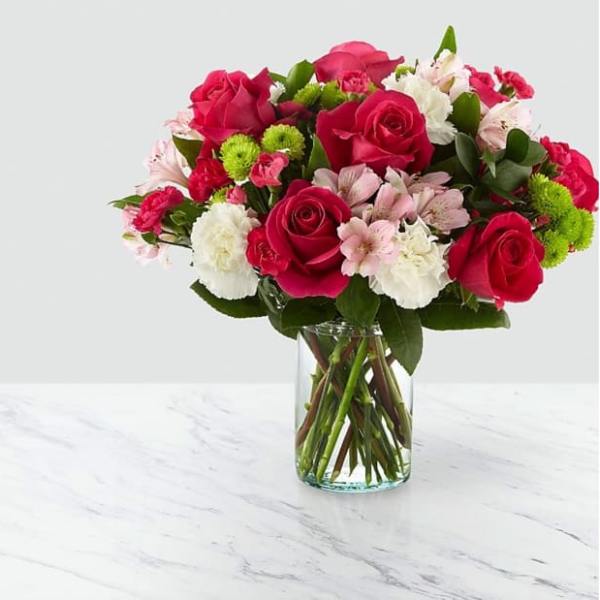 Bouquet of pink roses, white flowers, and green pompons in a glass vase