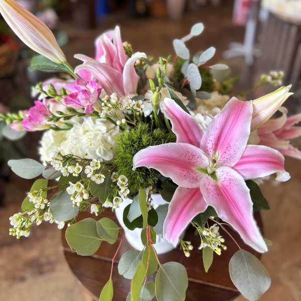 Pink lilies and white filler flowers in a white vase