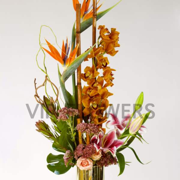 Tall tropical flower arrangement in a gold vase with orange and pink blooms