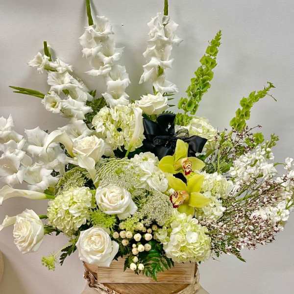 White floral arrangement with roses, orchids, and tall gladiolus in a wooden box