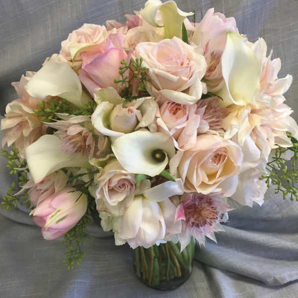 Bouquet of pale pink roses, white calla lilies, and blush flowers in a glass vase