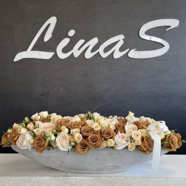 Long low arrangement of cream and tan roses in a shallow gray container