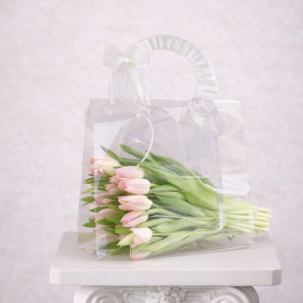 A wrapped bouquet of pale pink tulips in a clear gift bag