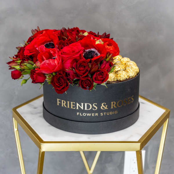 Red roses and poppies in a black round box with gold chocolates