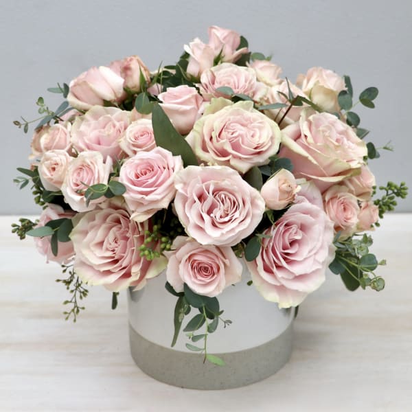 Pink roses arranged in a round white vase with greenery