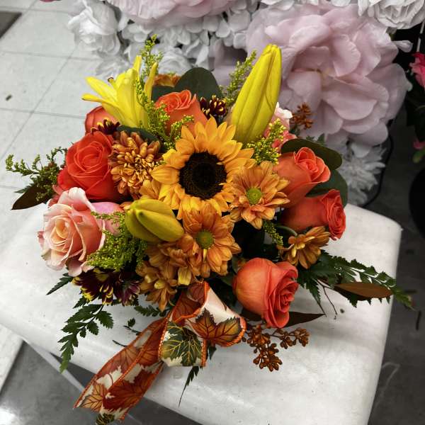 Bouquet of orange roses, sunflowers, and yellow lilies with a fall ribbon