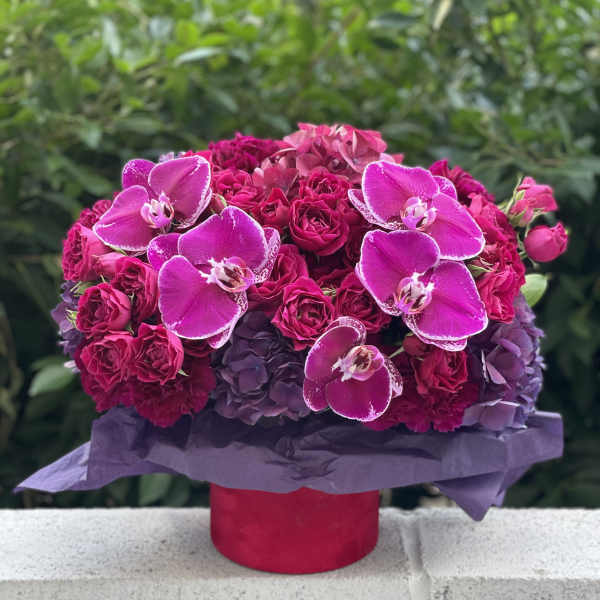 Pink roses and orchids arranged in a round box