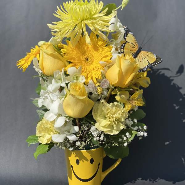 Yellow flower bouquet in a smiley-face mug with butterfly accents