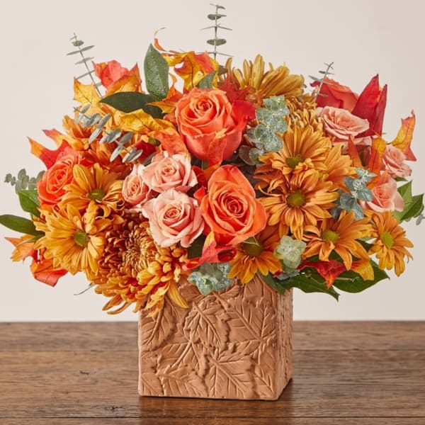 Autumn bouquet of orange roses and mums in a leaf-patterned vase