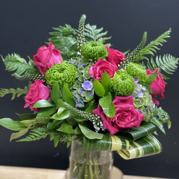 Vase arrangement of hot pink roses, green mums, and hydrangea with looped variegated leaves in a clear glass vase